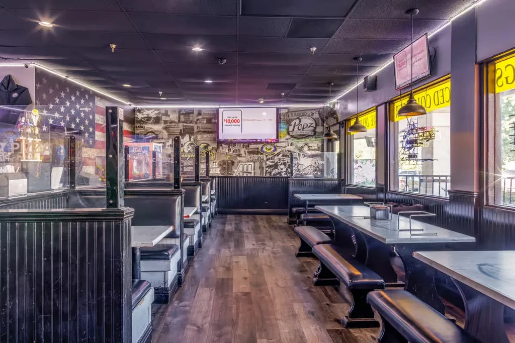 Empty casual restaurant interior with dark booths, communal tables, flag mural.