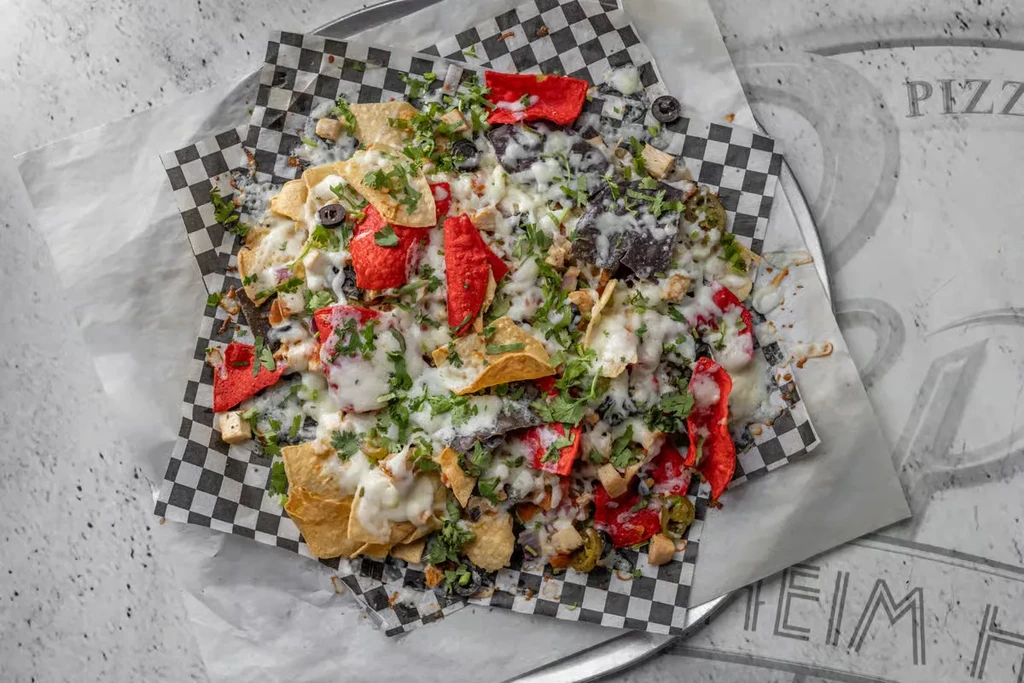 Piled nachos with cheese, chicken, olives, jalapeños, and colorful chips.