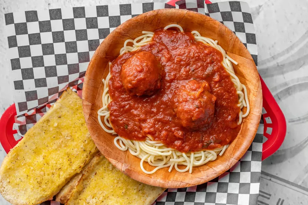 A bowl of spaghetti with meatballs and two slices of garlic bread.