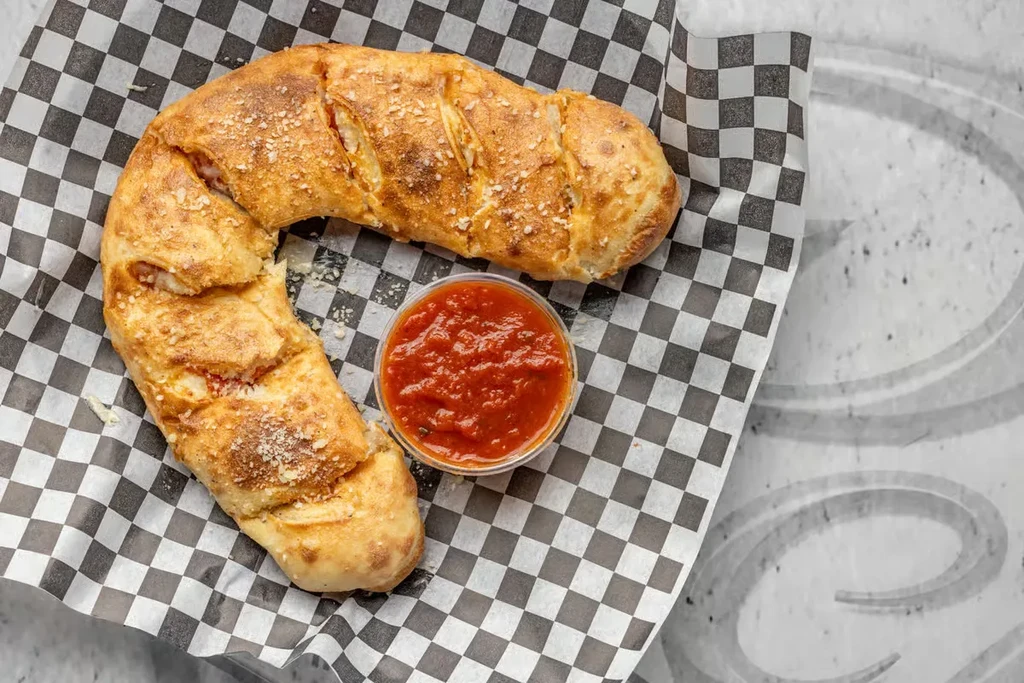 Golden crescent calzone with cheesy filling, Parmesan, herbs, and marinara sauce.