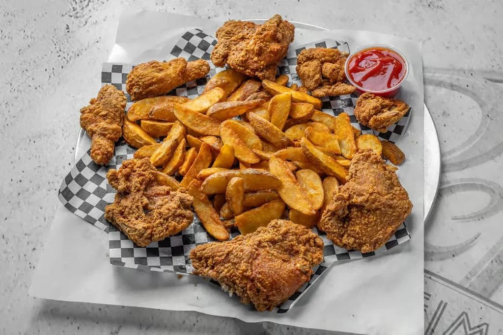 Golden-brown fried chicken and potato wedges with ketchup on a tray.
