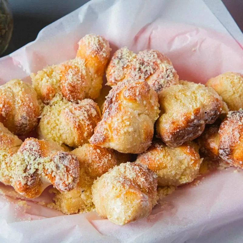 Pile of golden-brown savory bread knots with cheese topping in pink parchment.