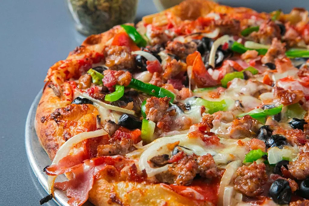 Close-up of generously topped pizza with sausage, bacon, and vegetables.