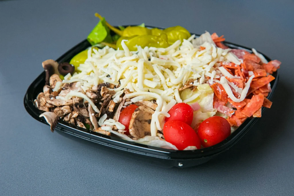 Salad with cheese, pepperoni, mushrooms, tomatoes, and peppers in takeout.