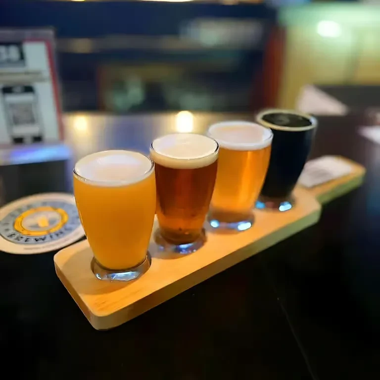 Four distinct beers on a wooden flight paddle, from light to dark.