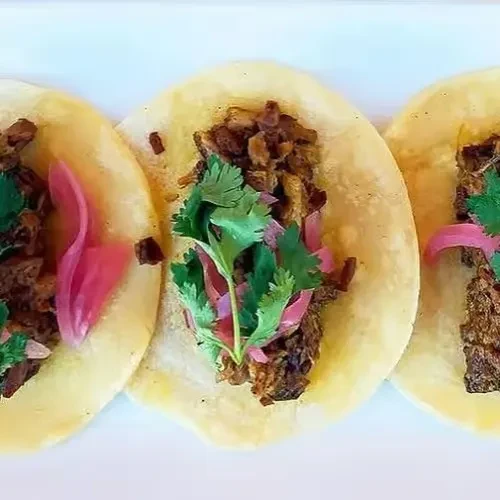 Three tacos with shredded meat, green cilantro, and pink pickled onions.