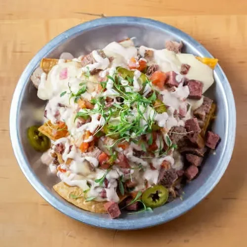 Close-up of loaded nachos with meat, cheese, tomatoes, herbs, and jalapeños.