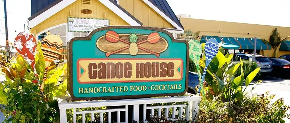 Vibrant "Canoe House" restaurant sign, tropical foliage, and yellow building.