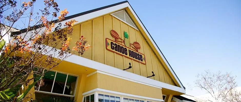 Yellow Canoe House building exterior with paddles and pineapple sign, blue sky.
