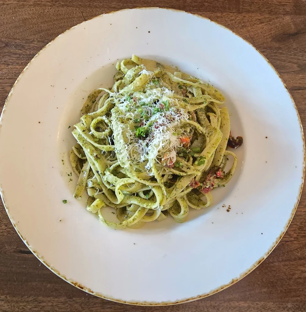 Fettuccine with green pesto, Parmesan, herbs on a wooden table.