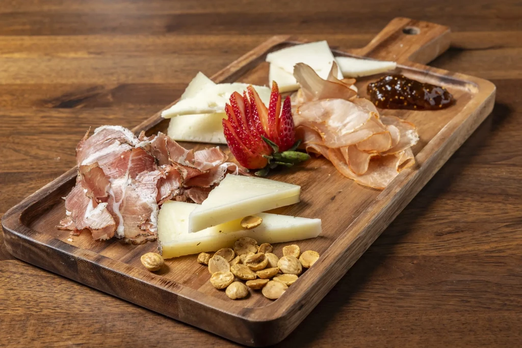 Wooden charcuterie board with cured meats, cheese, strawberry, jam, and nuts.