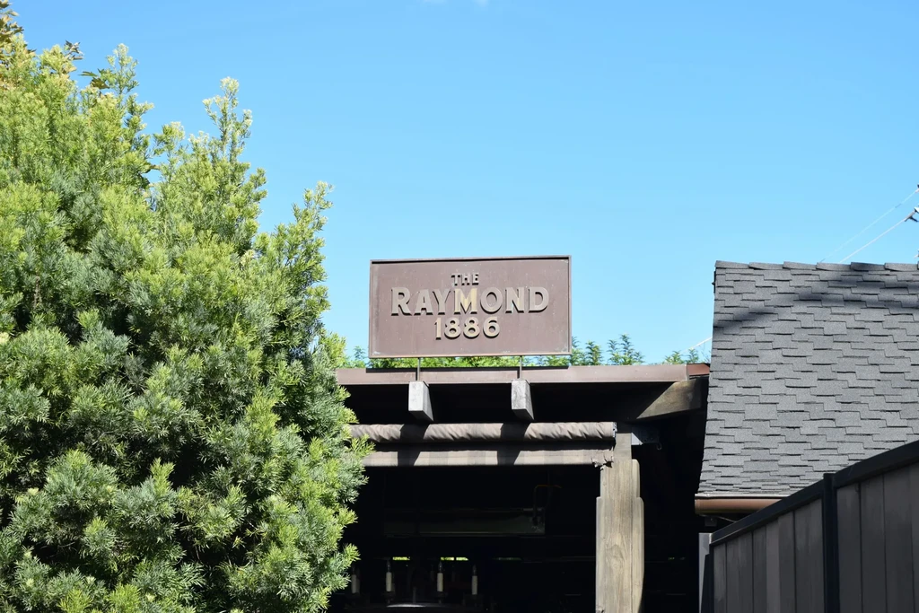 Bronze "THE RAYMOND 1886" sign above a building entrance, with trees.