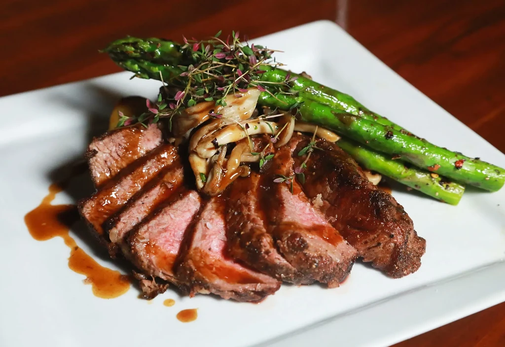 Sliced medium-rare steak with asparagus, mushrooms, and thyme on a white plate.
