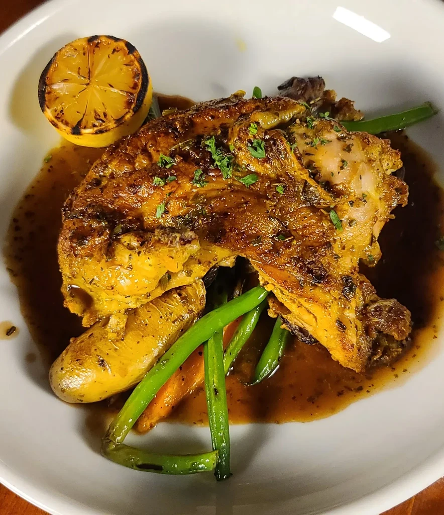 Roasted chicken, string beans, potato, charred lemon on a white plate.
