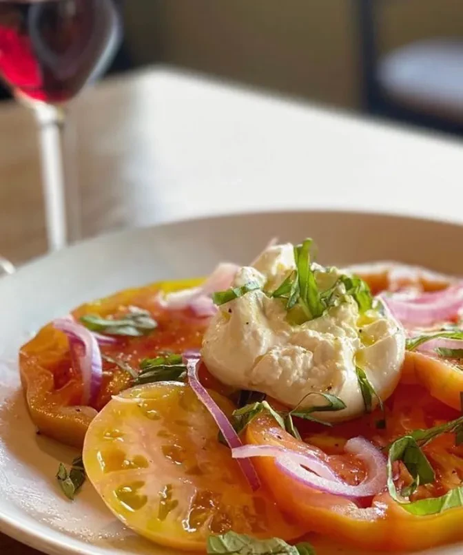 Close-up of heirloom tomato salad with burrata, basil, red onion, olive oil.