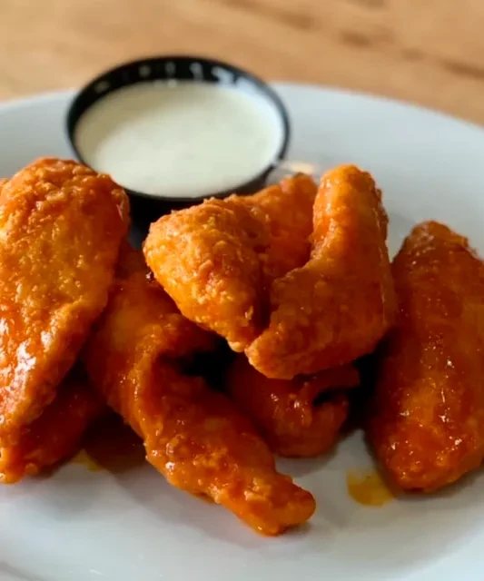 Buffalo chicken wings with orange-red sauce and creamy dip on a plate.