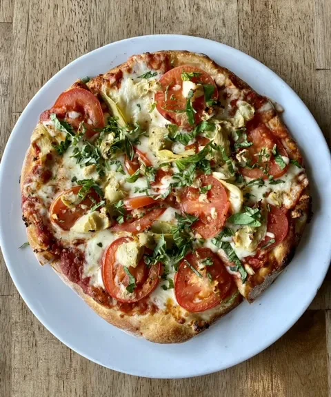Freshly baked pizza with cheese, tomatoes, artichokes, basil on wood.