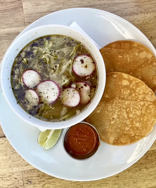 Overhead view: Light green soup, radishes, tostadas, salsa, and lime.