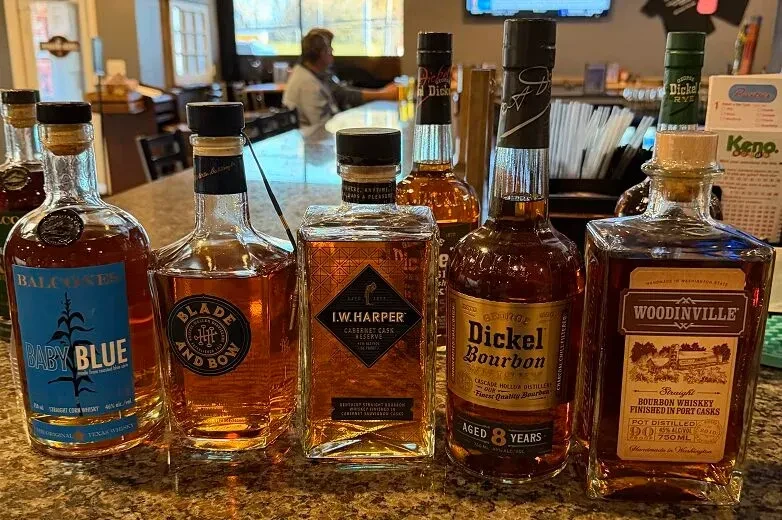 Six distinct whiskey and bourbon bottles lined up on a bar counter.