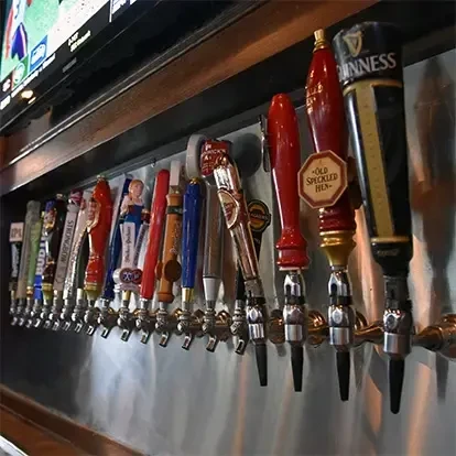 A row of various beer tap handles with a TV playing sports.