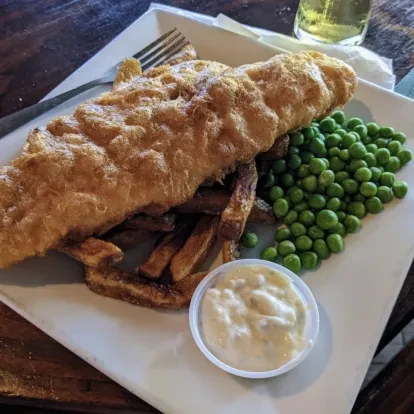 Golden battered fish and chips, peas, and tartar sauce.