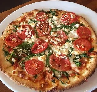 Golden-crusted pizza with tomatoes, crumbled cheese, and greens on a plate.