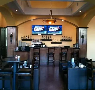 Empty restaurant bar: golden walls, stocked counter, flat-screen TVs, dining tables.