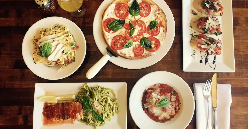 Top-down view of a wooden table with various colorful Italian dishes.