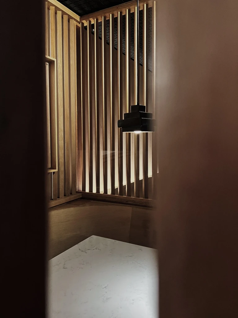 Contemporary restaurant interior with warm backlit wood slats and pendant light.