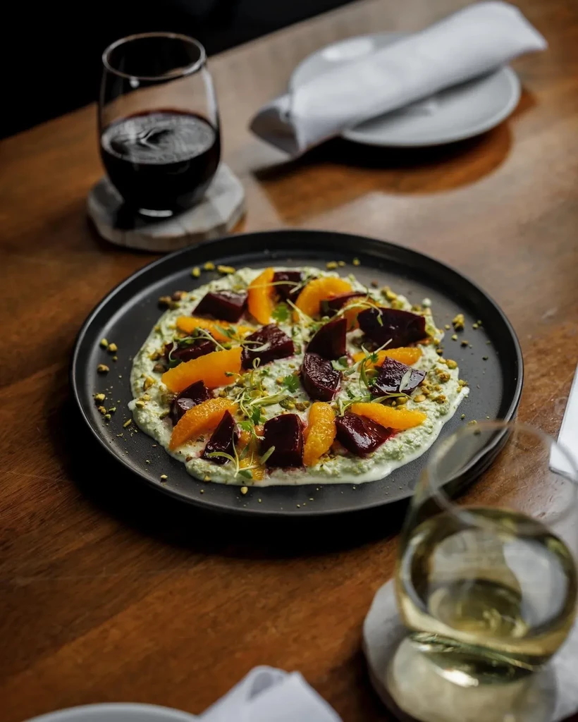 Plated dish with green base, beets, orange, pistachios, and microgreens.