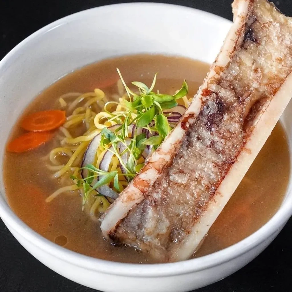 Upright roasted bone marrow ramen with noodles, carrots, and microgreens.