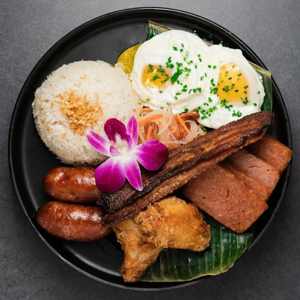 Overhead view: Rice, eggs, bacon, Spam, sausages, fried chicken, orchid.