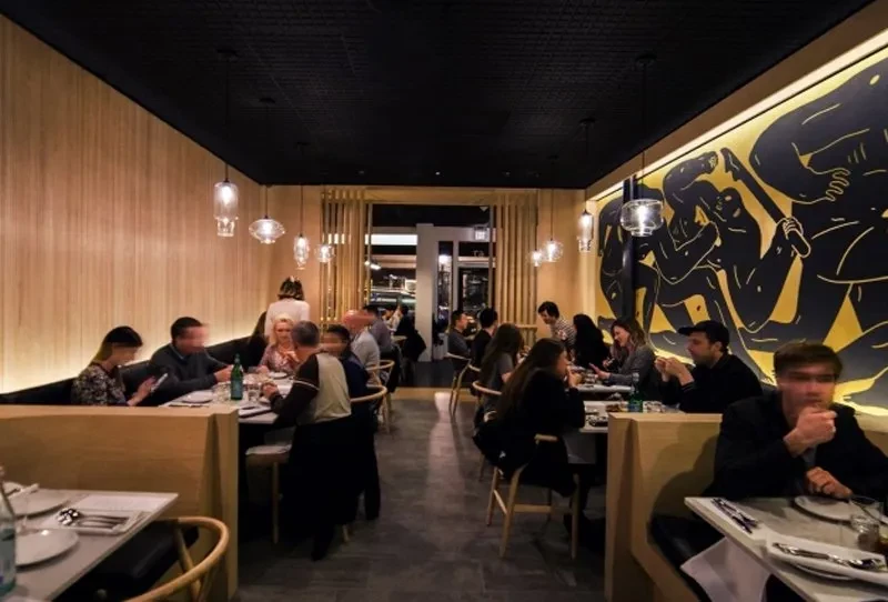 Modern restaurant interior: warm lights, black and gold mural, diners.