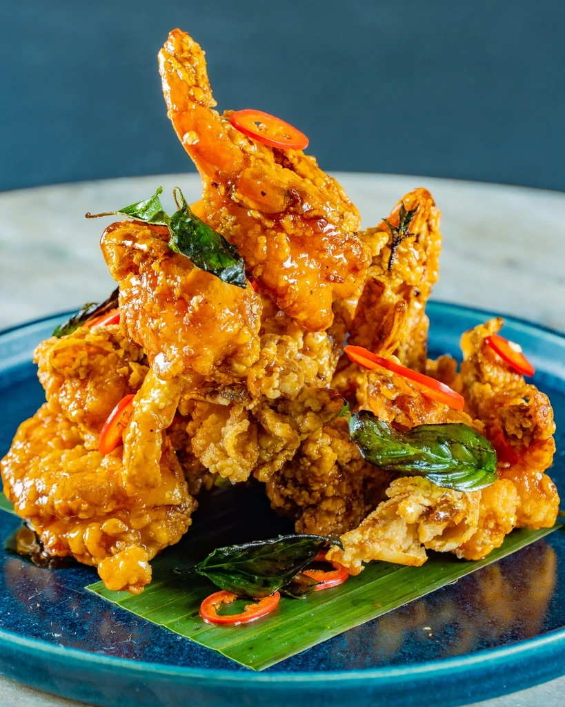 Crispy, orange-glazed chicken/prawns garnished with chilies on a banana leaf.