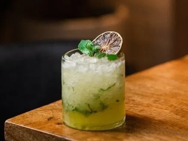 Lime green cocktail with crushed ice, mint, and dried citrus slice.