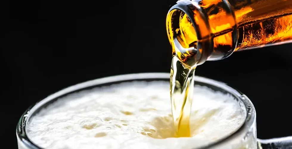 Golden beer pours from amber bottle into glass, creating frothy head.