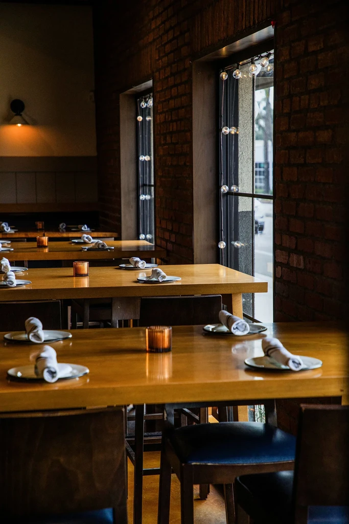Rows of set wooden tables in a warm, brick-walled restaurant.