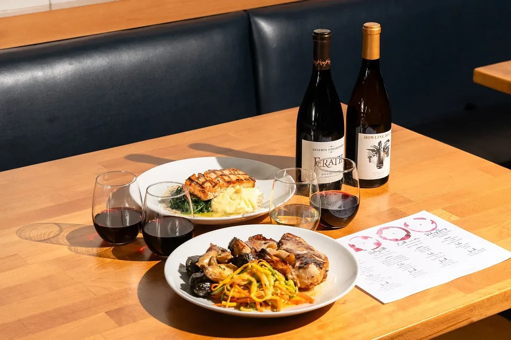 Restaurant table with plated fish, meat, wine, and a tasting guide.