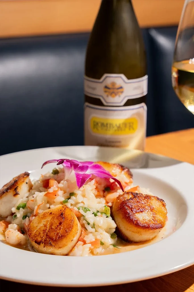 Seared scallops and risotto, orchid garnish, Rombauer wine in a restaurant.