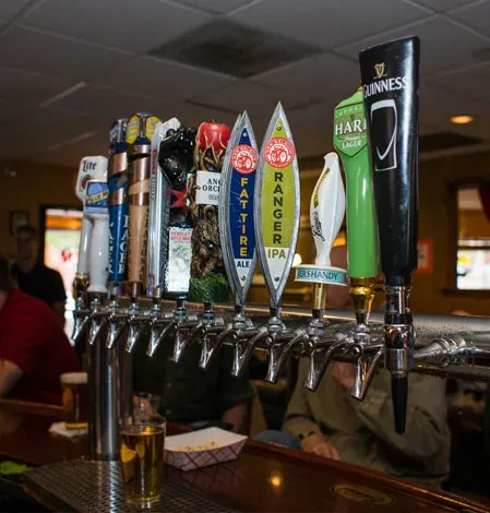 Close-up of beer taps with a drink and snacks on a bar.