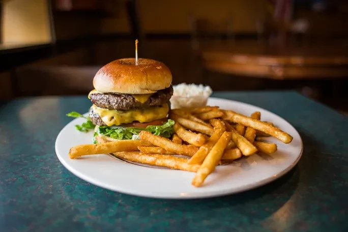 Double cheeseburger with fries and a side on a white plate.