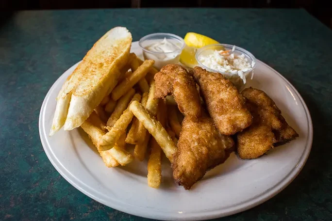 Fried fish, french fries, garlic bread, tartar sauce, coleslaw, lemon.