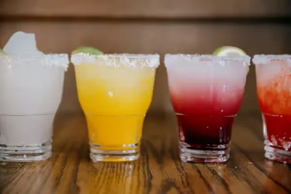 Four colorful margaritas with salt rims on a wooden surface.