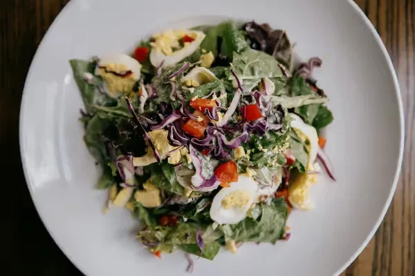 Vibrant salad with greens, red cabbage, tomatoes, eggs, and creamy dressing.