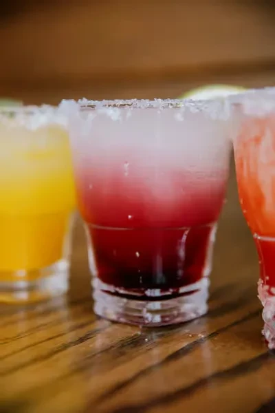 Three colorful gradient drinks in tumblers rimmed with salt or sugar.