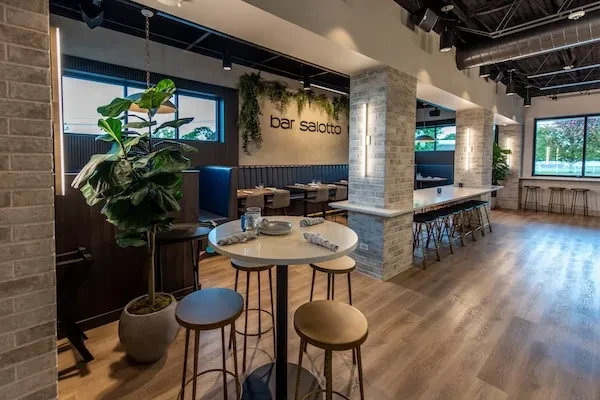 Modern restaurant interior with brick, wood, and a large plant.