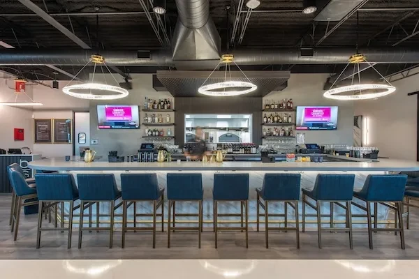 Modern bar interior with a long counter, stools, and televisions.