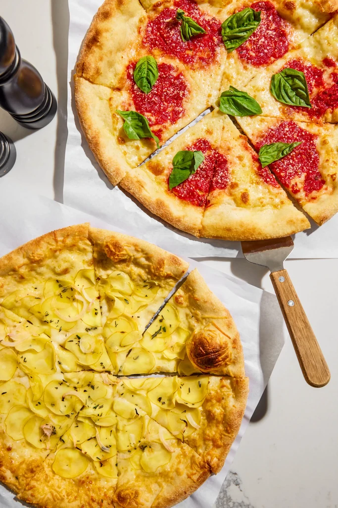 Overhead shot of Margherita and potato pizzas on parchment paper.