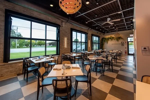 Modern restaurant dining area with checkerboard floor and exposed brick.