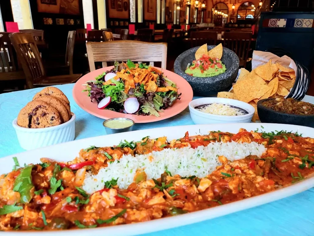 Mexican food spread with meat, salad, guacamole, beans, and chips.